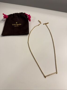 kate spade gold bar pendant necklace with brown pouch and pink drawstrings